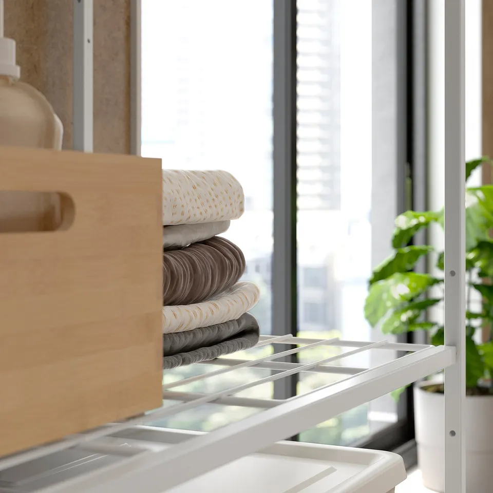 White JOSTEIN shelving unit with stacked towels and wooden drawer, indoor plant.