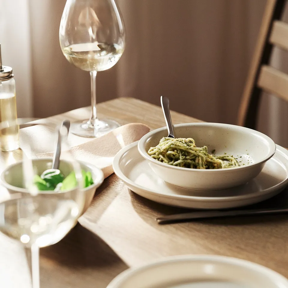 Rustic table setting with stoneware, food, and glass on wood table with chair.