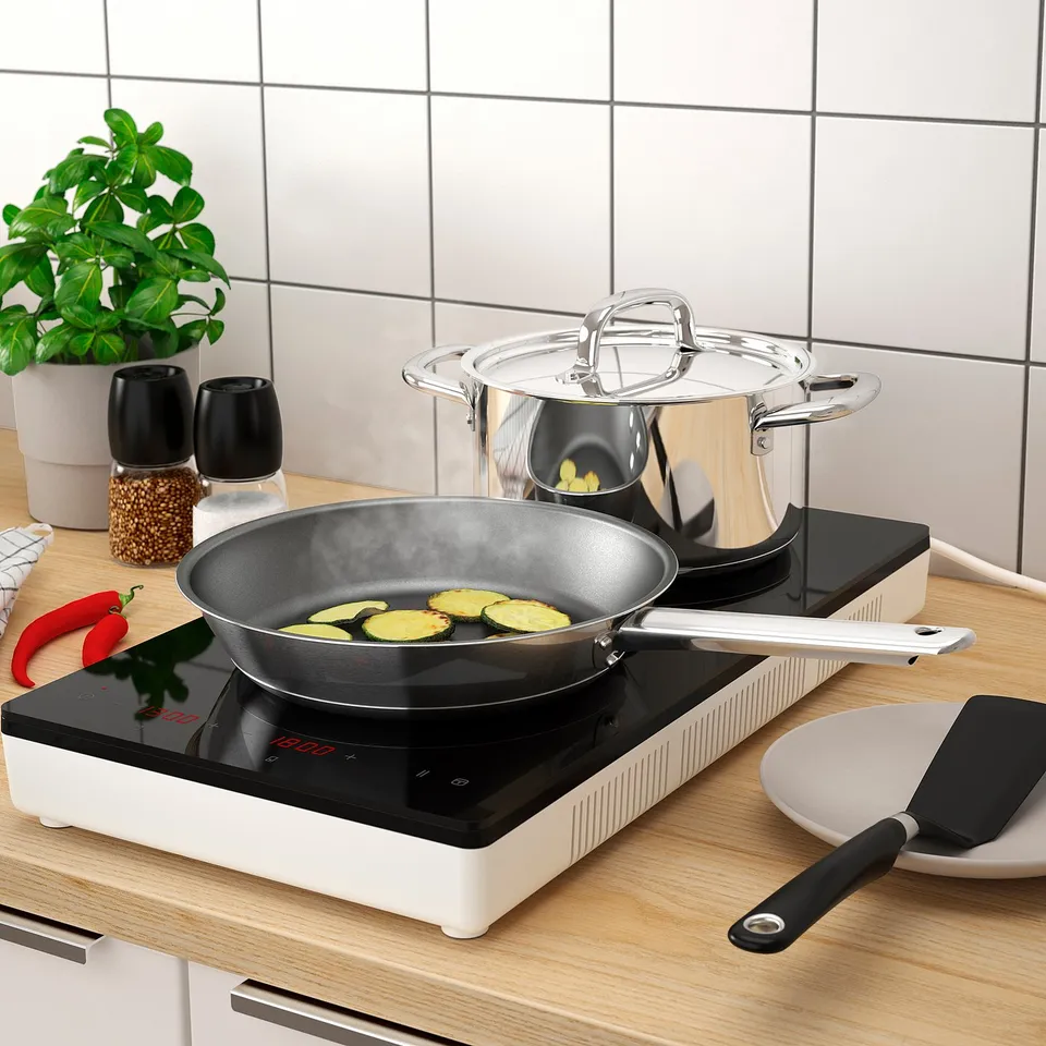 Modern kitchen scene with a portable induction hob cooking courgette slices. The hob has digital controls and a glass cover on a saucepan nearby.