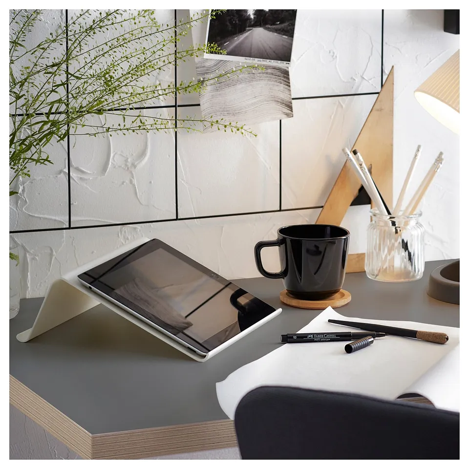 Modern desk setup with tablet, black mug, pens, and plant.