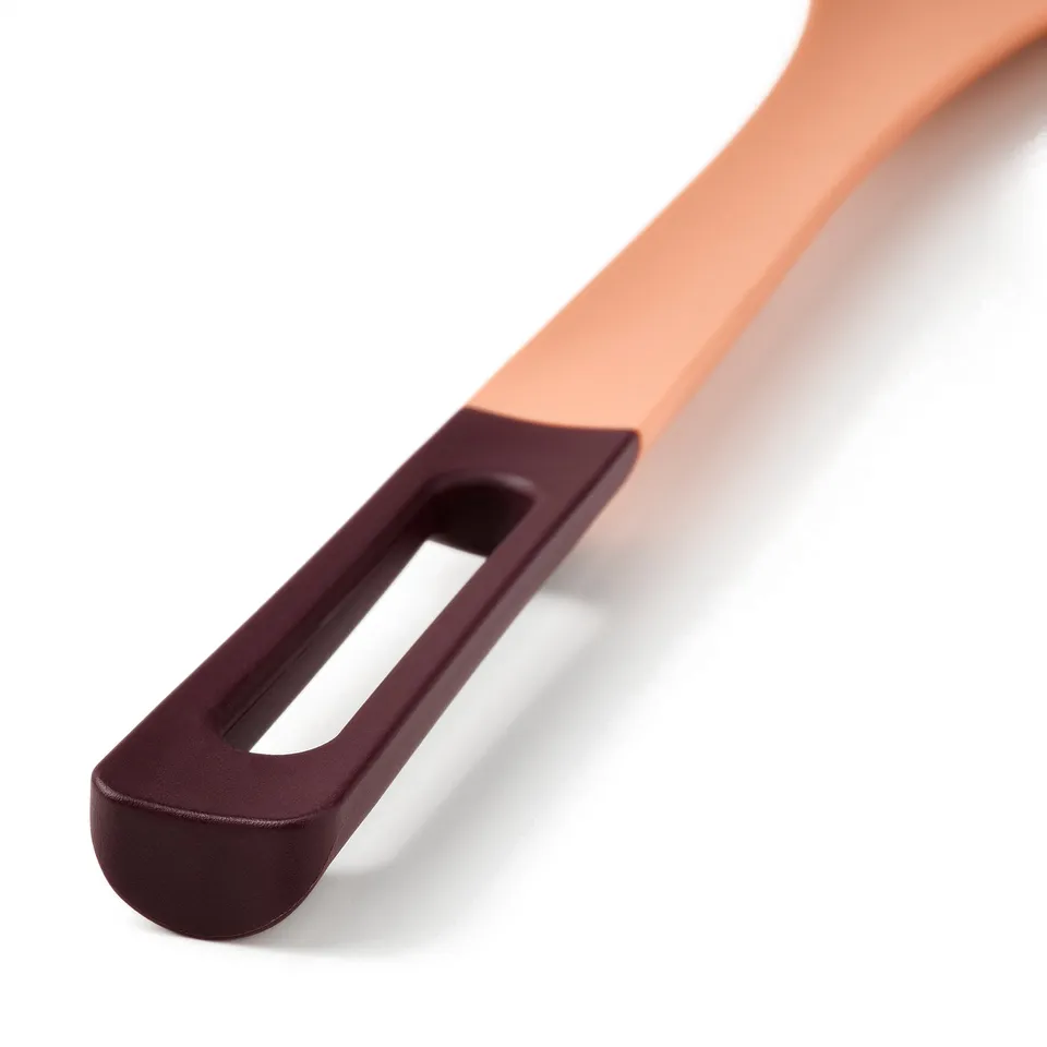A close-up of a peach-colored spoon with a dark handle, showcasing modern design and ergonomic grip.
