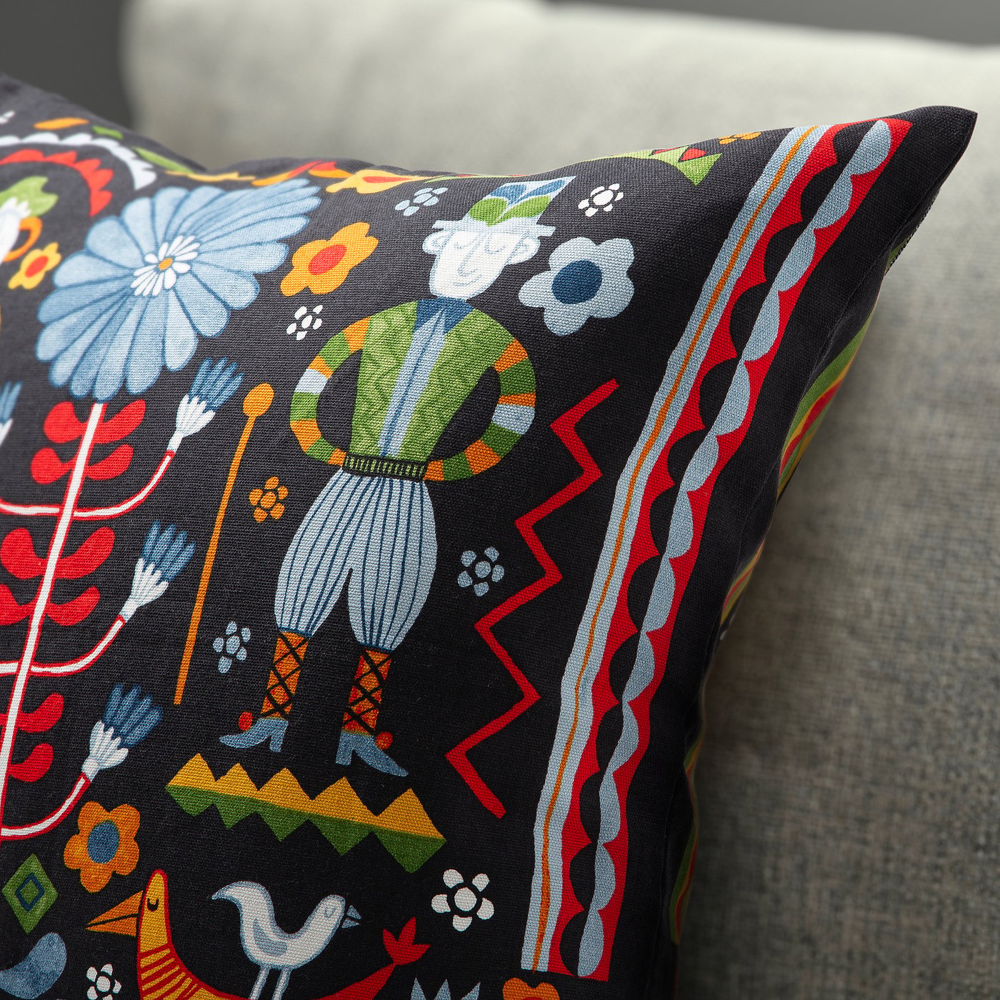 Vibrant, detailed cushion cover with floral patterns and traditional costumes on black fabric.