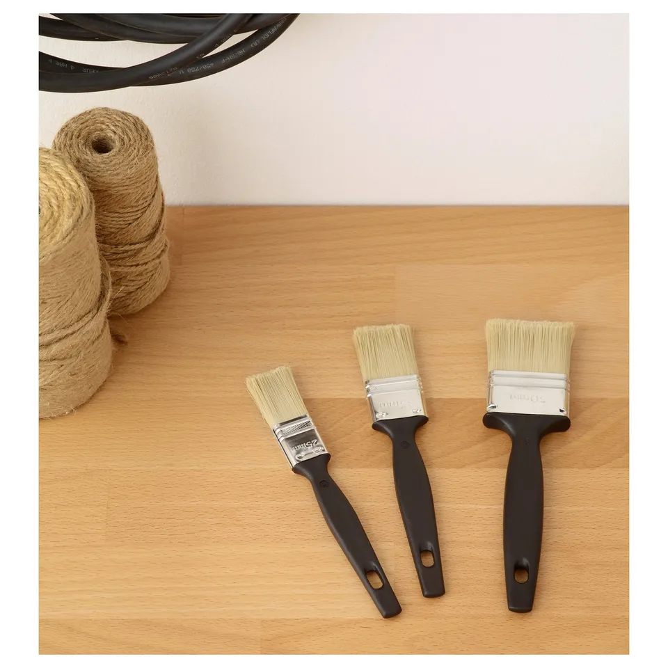 Three paint brushes of varying sizes lay on a wooden surface, accompanied by a coil of twine. Perfect for smooth paint application.