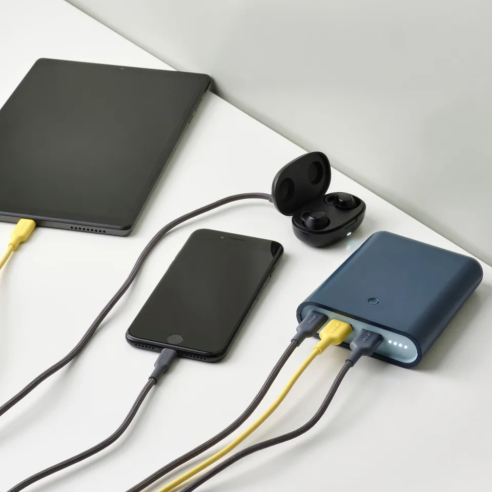 Power bank charges smartphone, tablet, and earbuds simultaneously. Multiple ports. On white surface.