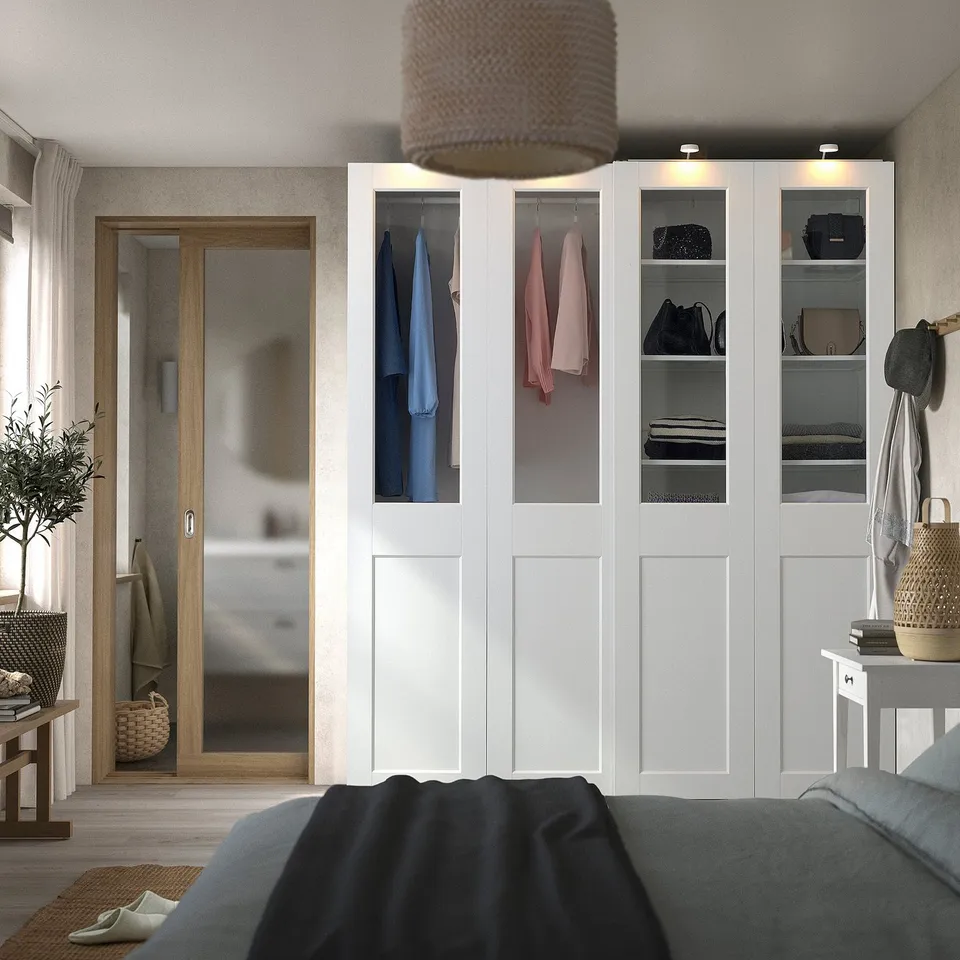 Bedroom with white PAX wardrobe, glass doors, grey bed, wooden mirror, wicker lamp, wall decor.