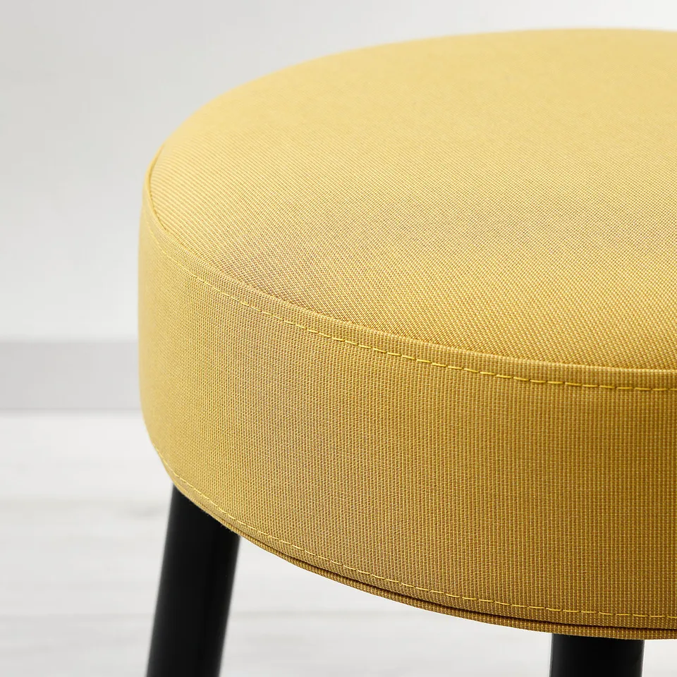 Close-up of a yellow upholstered stool, showing its smooth fabric and sleek metal base, highlighting its robust and stylish design.