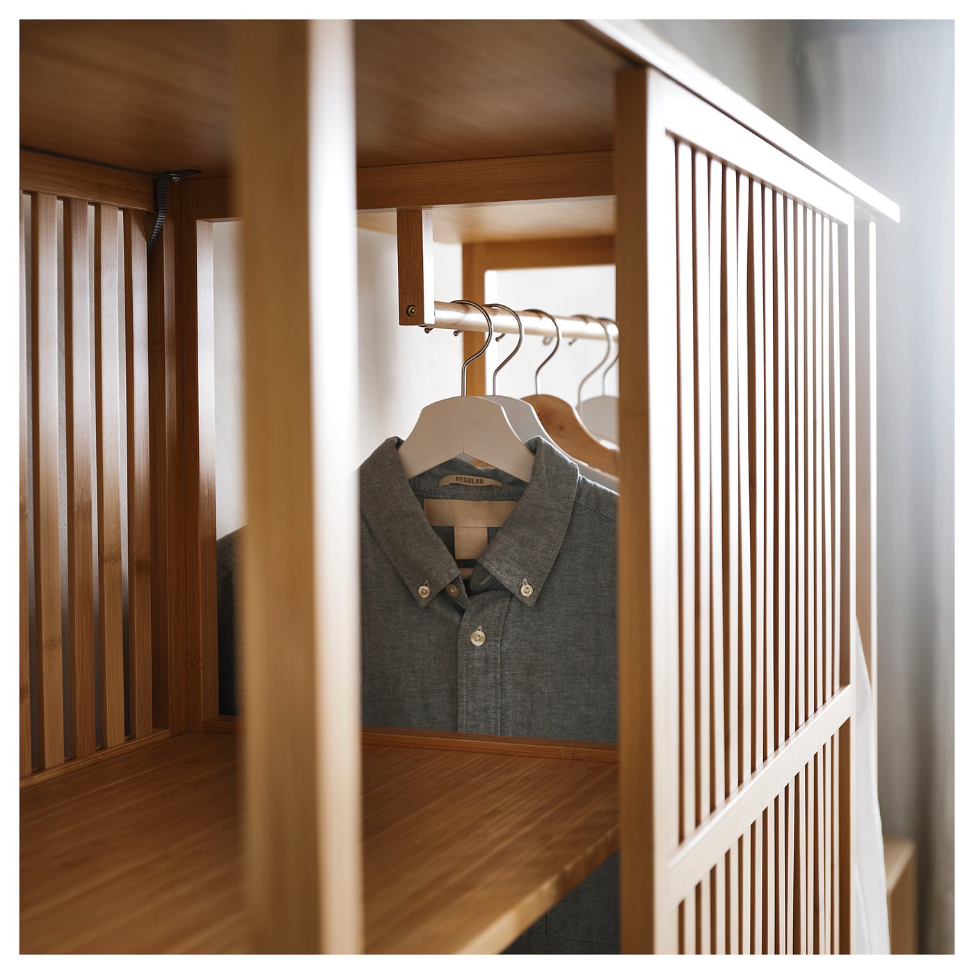 A NORDKISA wardrobe in natural bamboo. It sliding doors and hanging space where a grey shirt is visible. The design is minimalistic with clean lines.