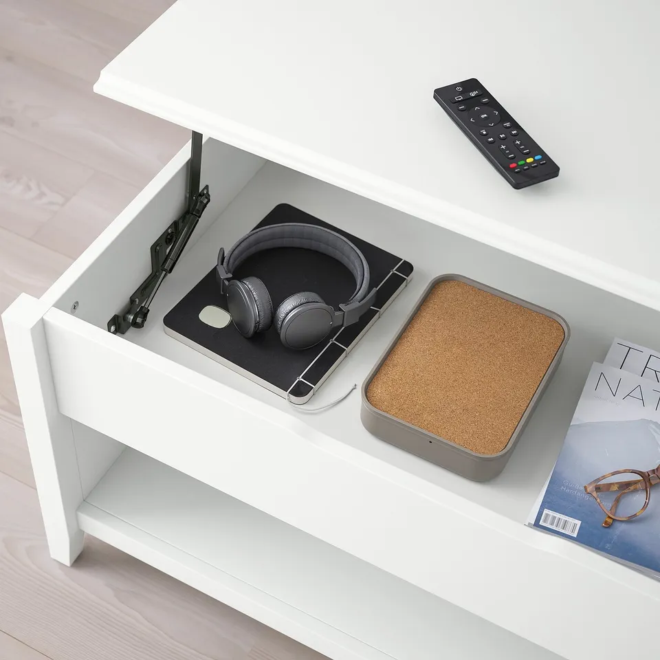 White VITTERYD coffee table with adjustable height and storage space. Headphones and remote seen on hidden shelf.