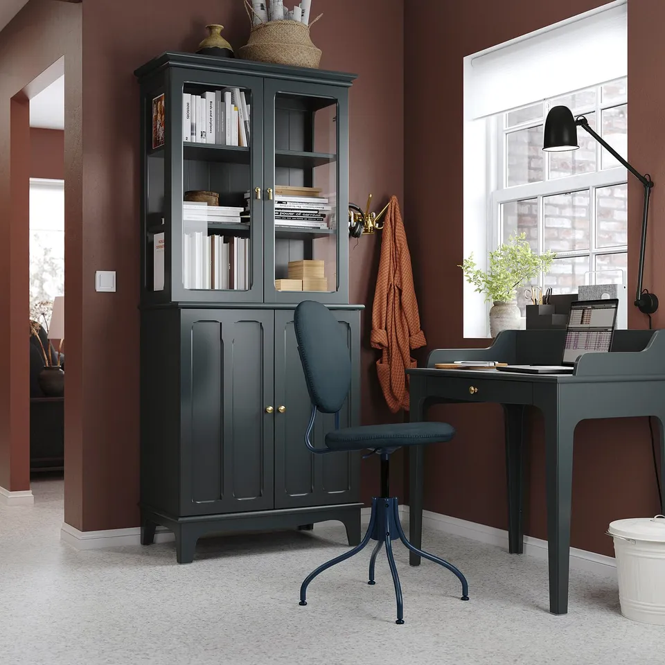 Home office with LOMMARP black cabinet, chair, and desk against maroon walls, featuring storage shelves and a glass door.