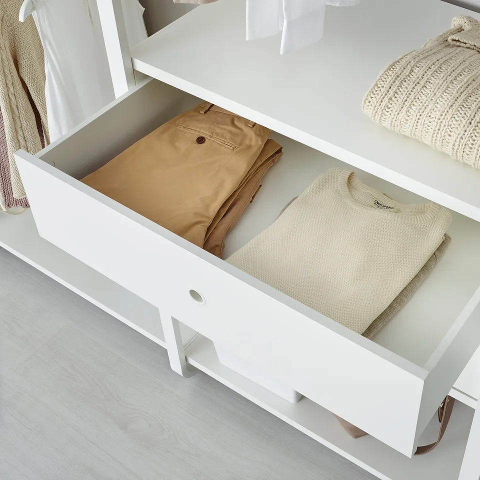Open white drawer from ELVARLI system showing neatly folded beige pants and a folded sweater. Drawers catch and close slowly.