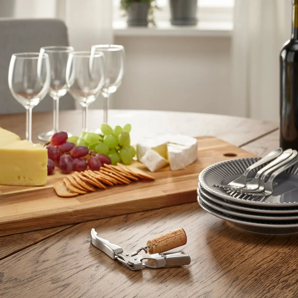 Cheese platter with crackers, grapes, wine glasses, and corkscrew.
