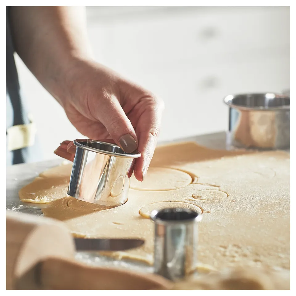 A person uses a silver cookie cutter to shape golden dough.