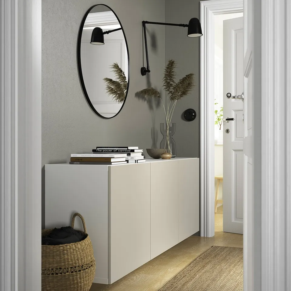 White BESTÅ sideboard with mirror reflecting plant and books in an entryway.