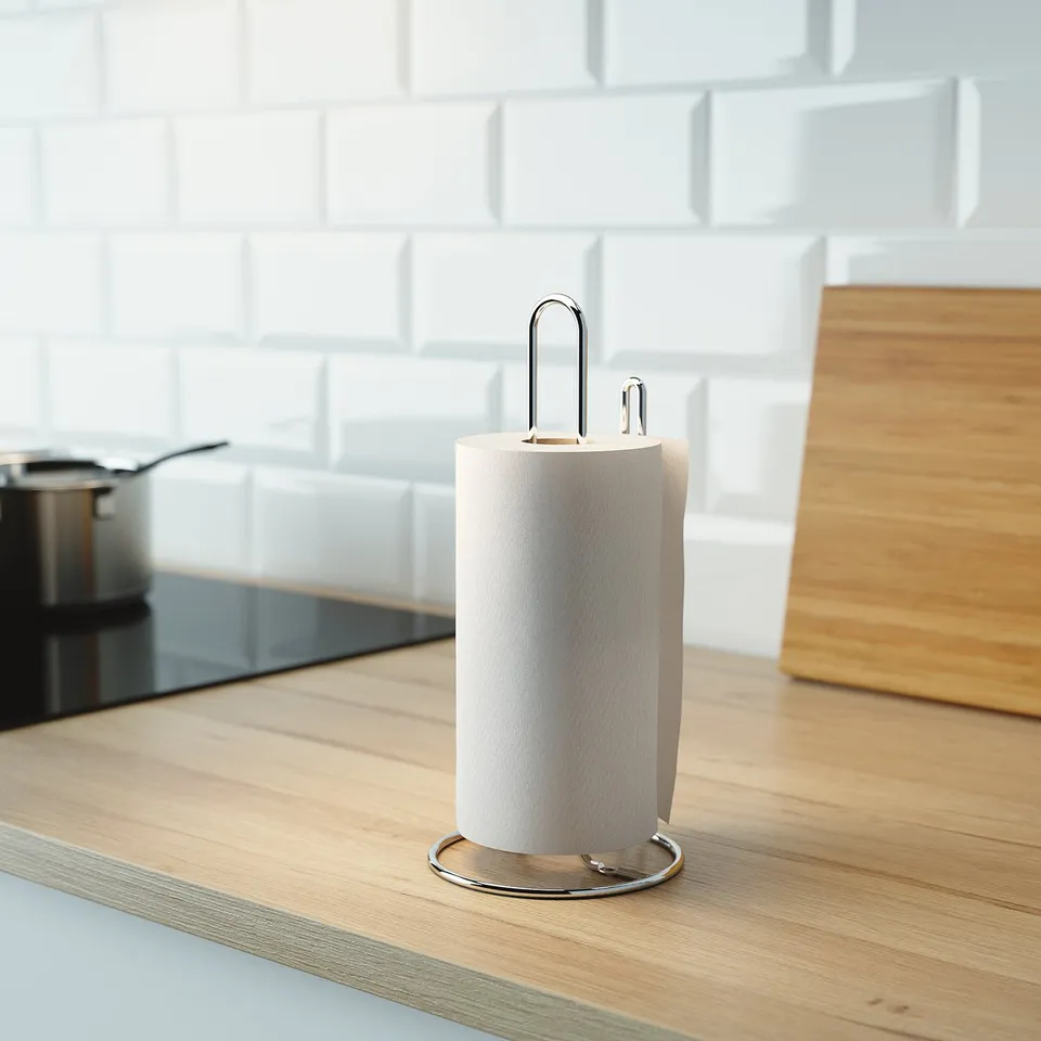 Kitchen counter with light wood surface; stainless steel paper towel holder stands centre, roll positioned for easy tear.