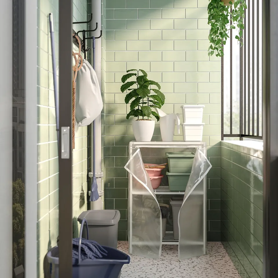 Balcony storage: JOSTEIN metal shelf, light green, square, with removable cover, potted plant, and supplies, near glass door.