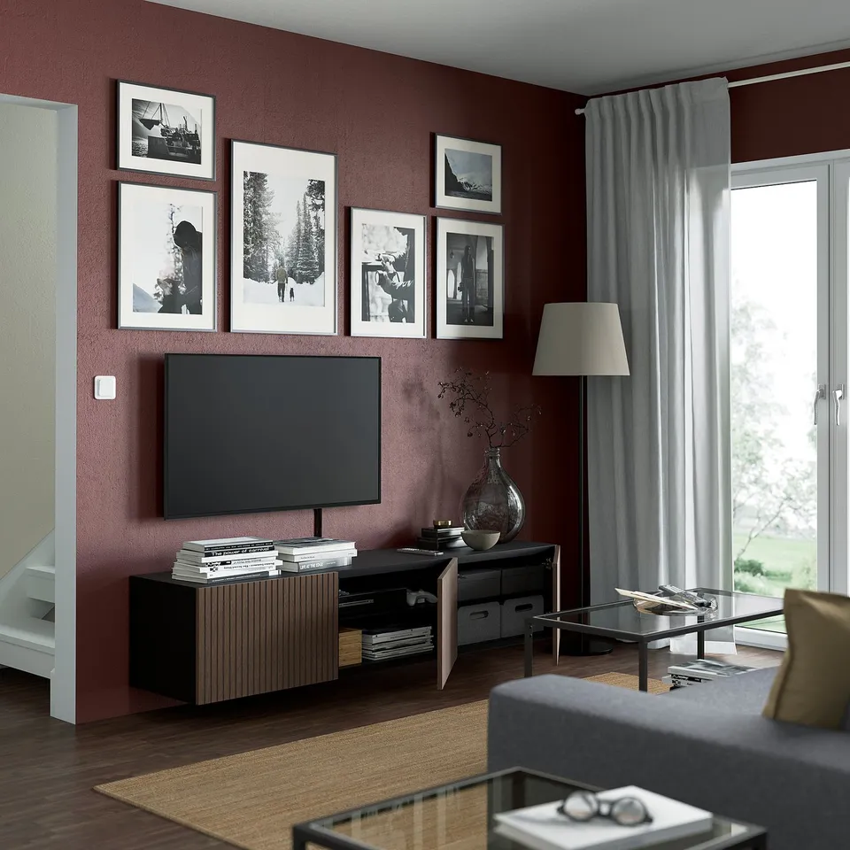 Modern living room with dark red walls, large tv, floor lamp, and framed pictures. A sofa, coffee table with books, and a glass vase adds comfort.
