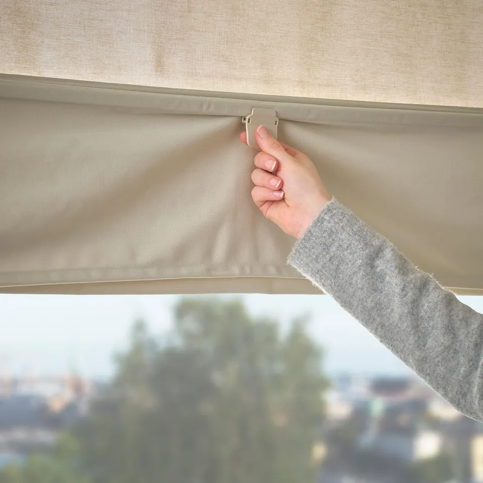 Person adjusting beige roman blind with magnetic control, offering privacy and light filtering.