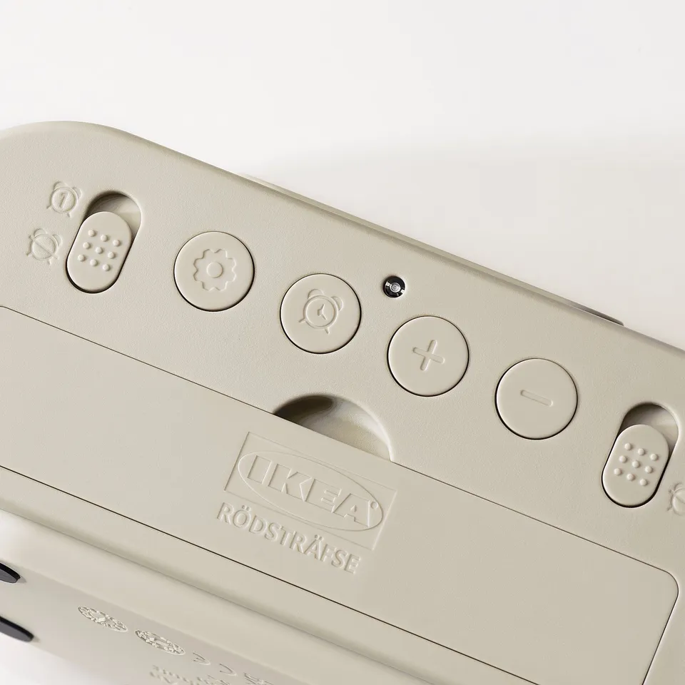 Beige alarm clock with IKEA logo, featuring buttons for time, alarm, and light controls, displayed on a light background.