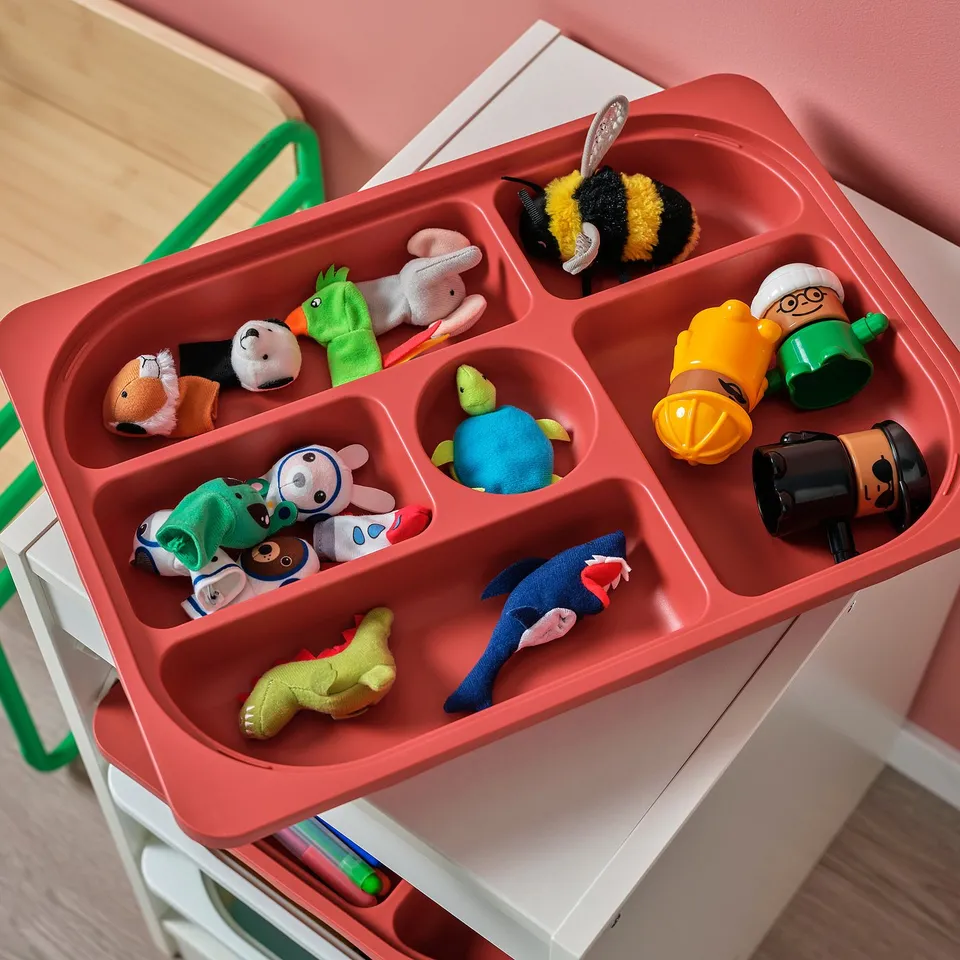 Red storage tray with multiple compartments holding various toys, including stuffed animals and figurines, organised neatly.