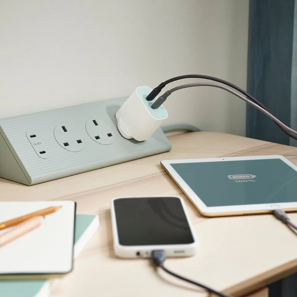 Wooden desk with a white SKOTAT extension cord, black phone, and tablet charging.