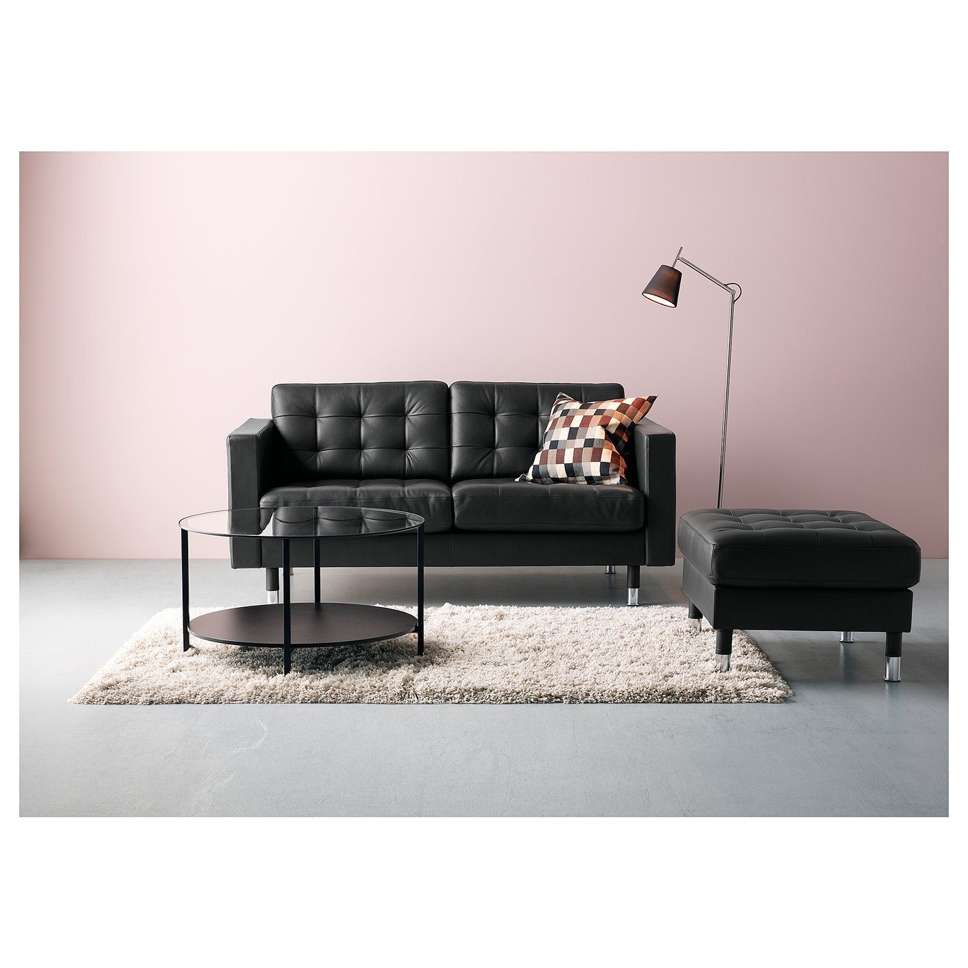 Modern living room with black leather couch, glass coffee table, footrest, and tall lamp on pink wall.