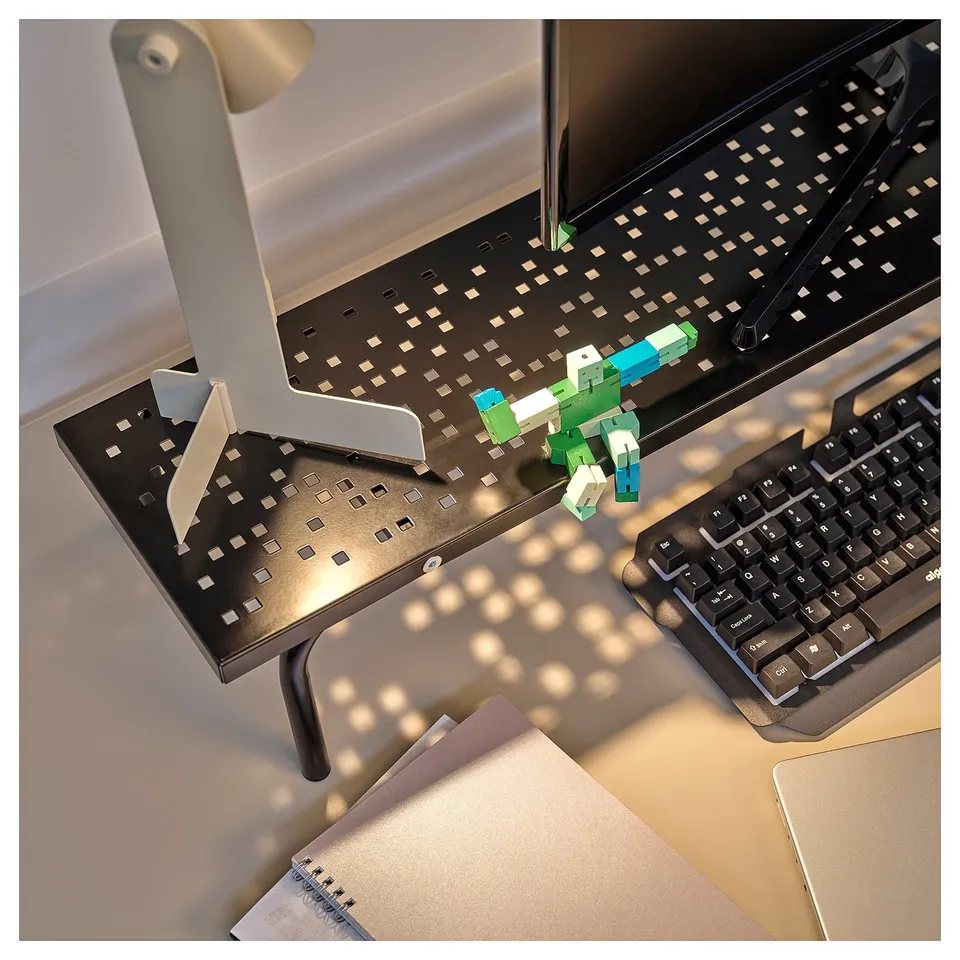 A gaming desk setup with a black monitor stand, a keyboard, and a colourful block robot toy, designed for ergonomic and organised gaming.
