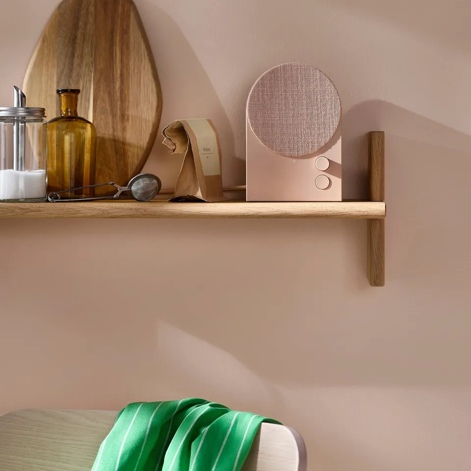 Wooden shelf with gold bluetooth speaker, green towel.