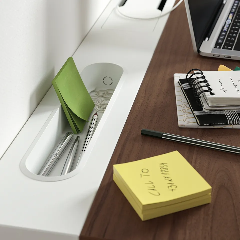Desk organised with a laptop, notebook, sticky notes, and pens. Green sticky notes are stored in a holder, signifying a well-organized workspace.