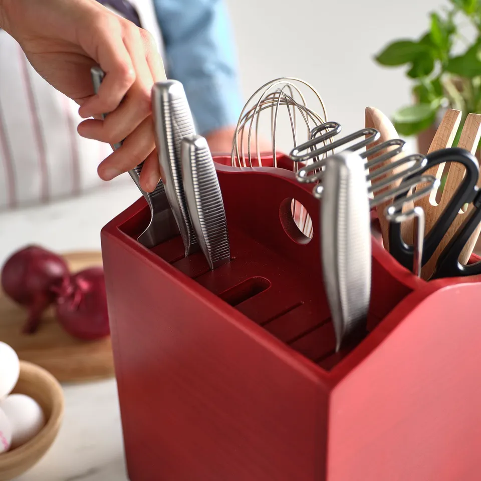 Hand reaches into red HAVSMAL wooden knife block, holding a knife. The block organises knives and utensils neatly.
