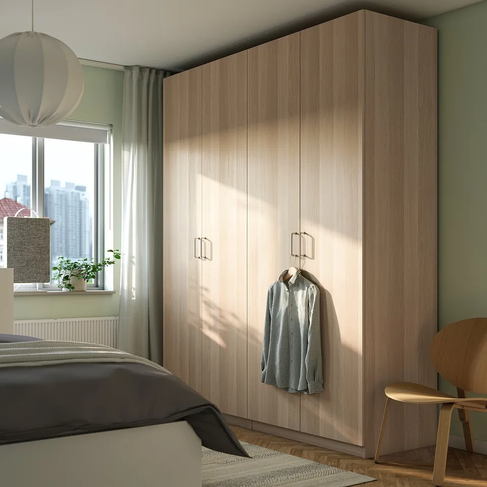 Modern bedroom with beige PAX wardrobe, striped shirt, bed, light, chair, window with cityscape.