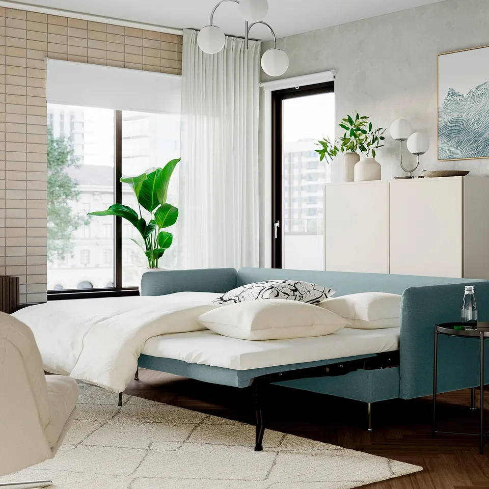 Modern bedroom with teal sofa-bed, white linens, big window, sheer curtains, cabinet, lights, and plant.