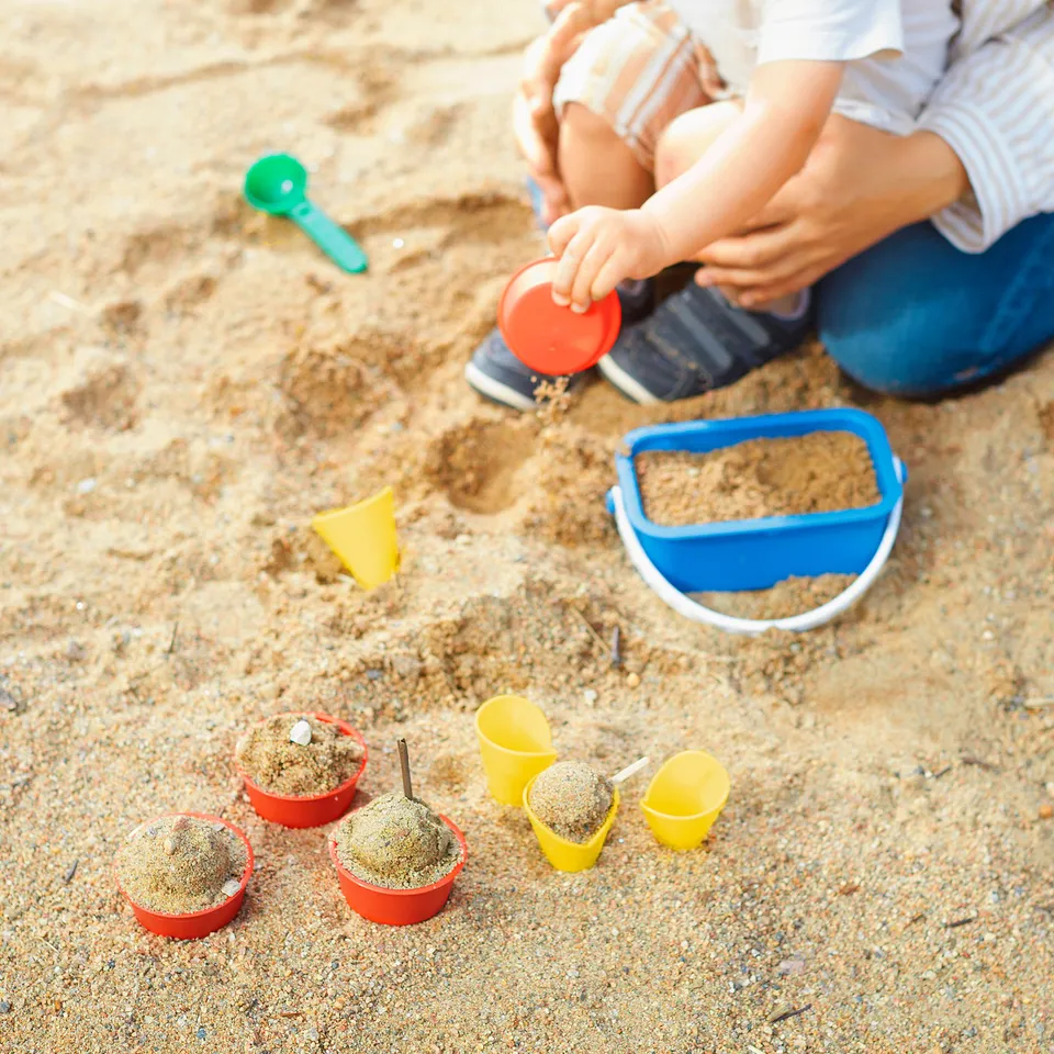 Child playing with colourful sand moulds on beach. Includes cups, cones, and scoop.