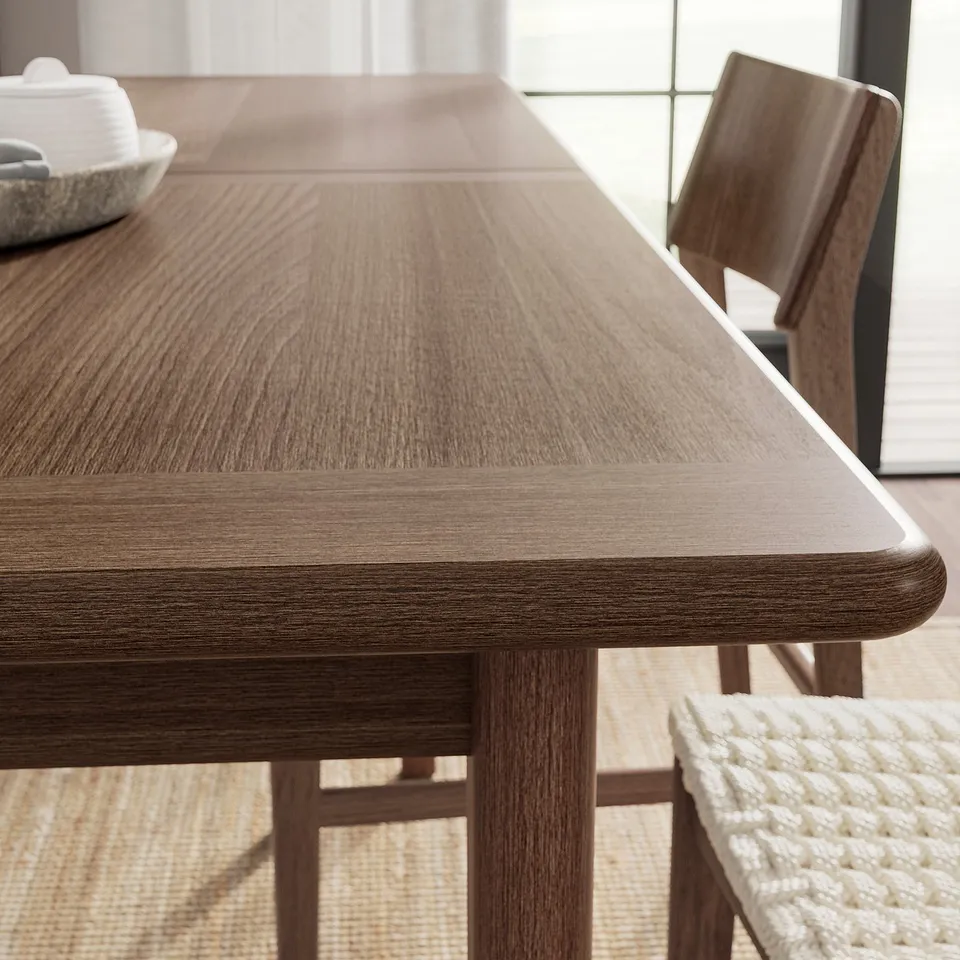 Modern wooden dining table with smooth, polished finish. Chair with woven seat and backrest visible on right.