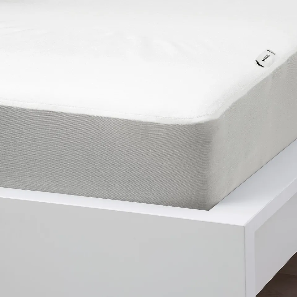 White mattress protector on bed, with waterproof, secure fit, and elastic edges.