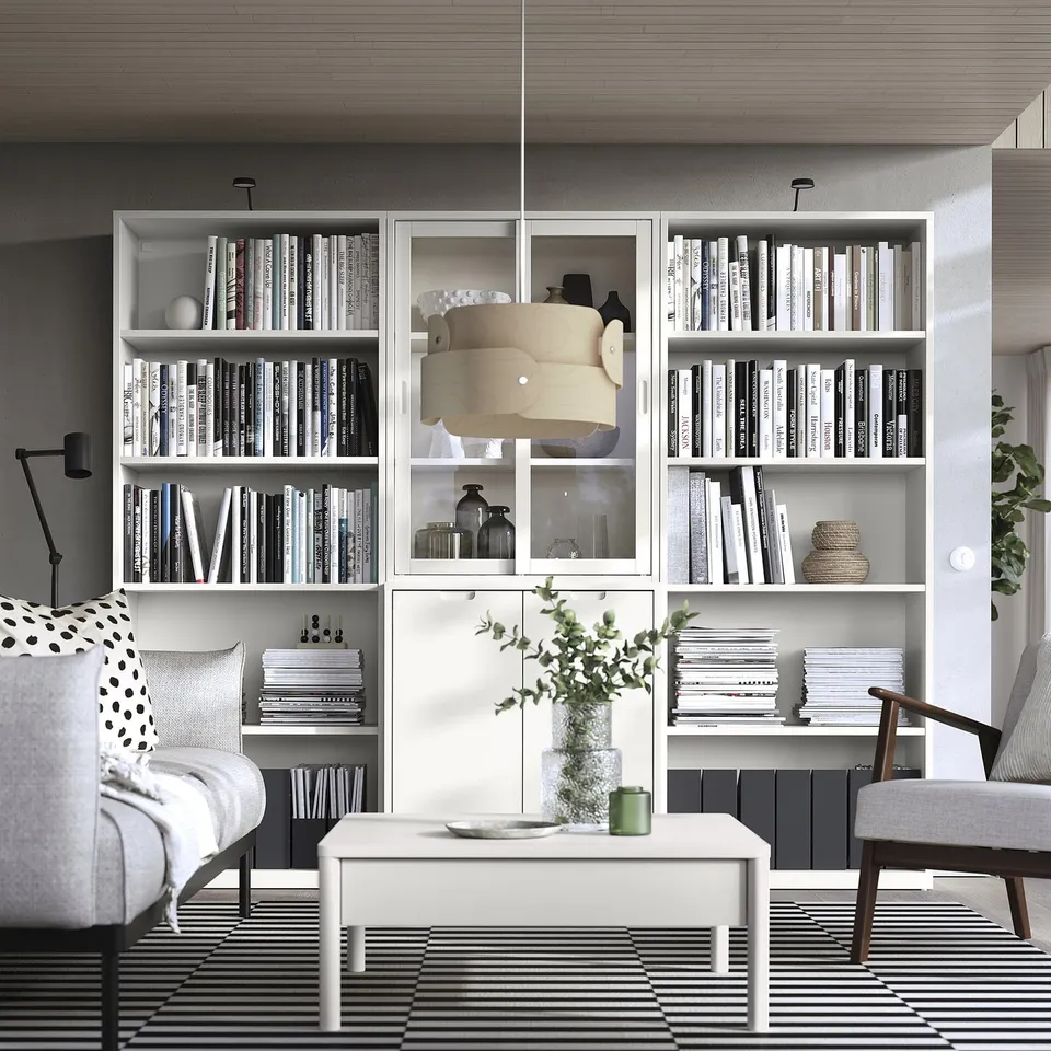 Modern living room with off-white TONSTAD coffee table, grey chairs, striped rug, large bookshelf filled with books, and decorative lamp.
