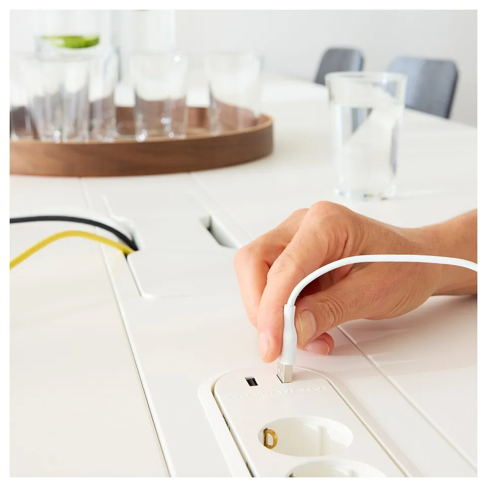Hand plugs white MITTZON cable into modular power socket on white conference table.