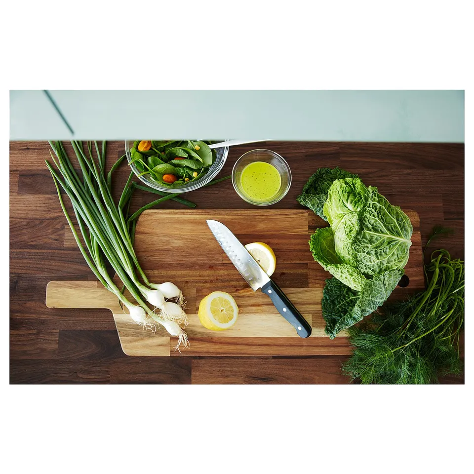 Wooden kitchen counter with cutting board, knife, veggies, bowl, and dressing.