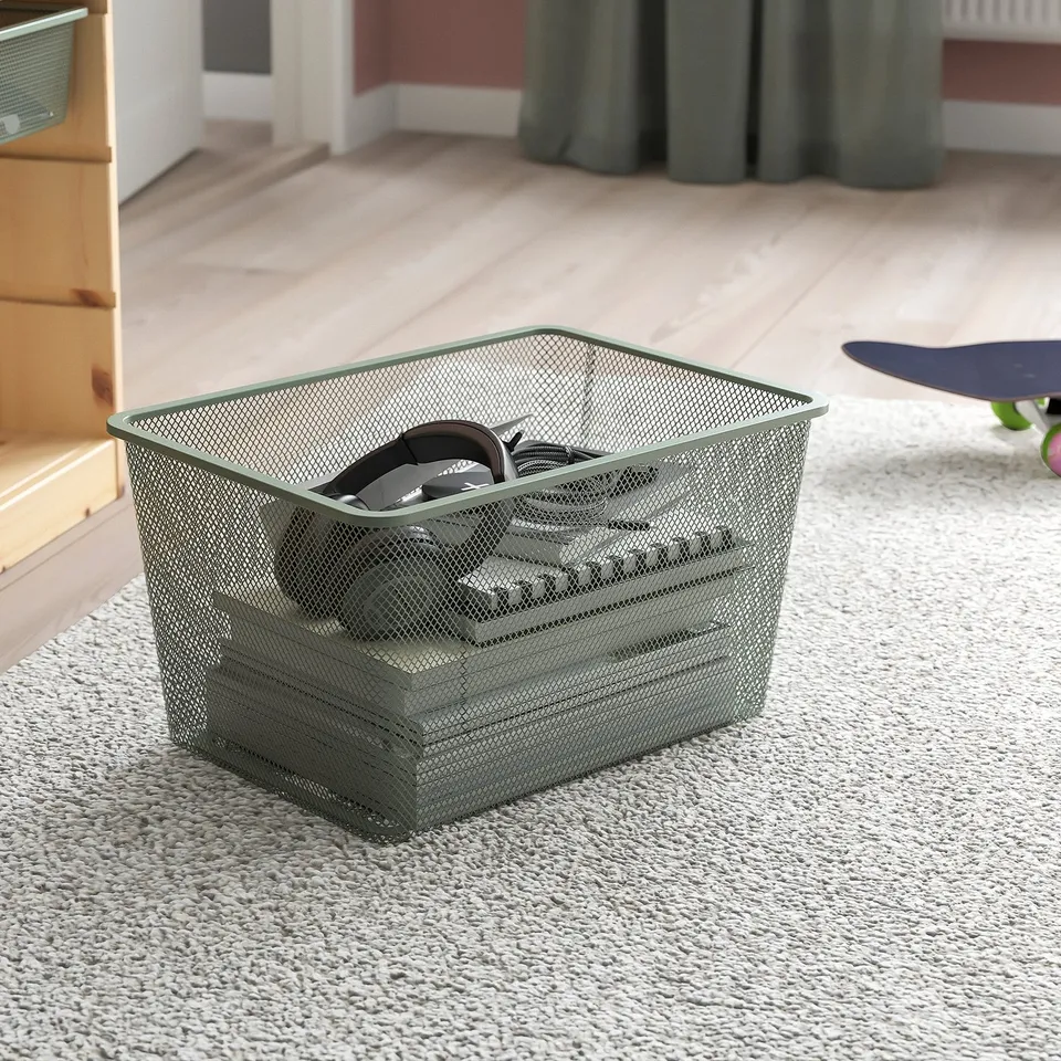 Mesh storage basket on carpet, holding headphones, part of TROFAST system.