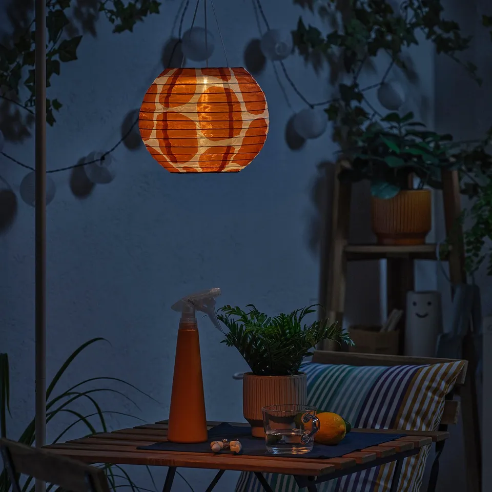 Orange lantern illuminates cosy patio with plant, glassware, and lemon. Stripes and cushions add to relaxed ambiance.