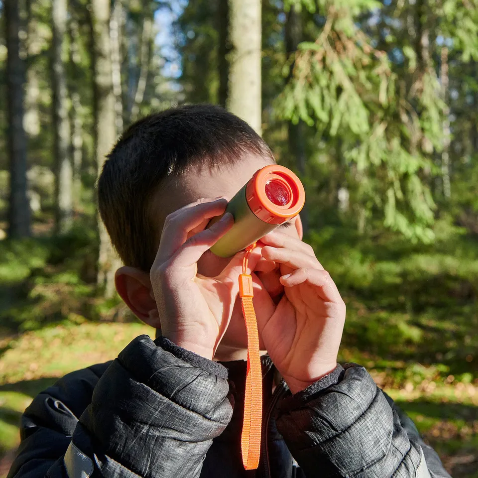 Boy in jacket uses orange telescope in forest.