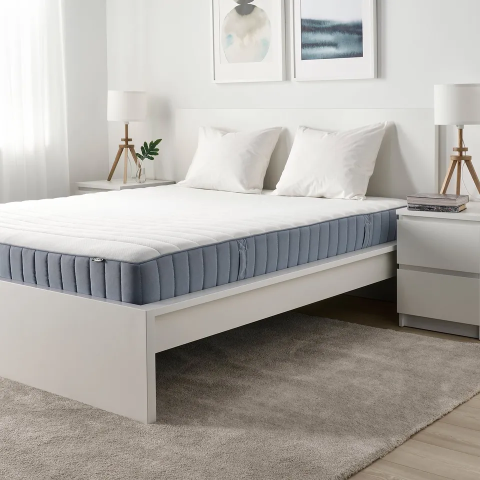 Modern bedroom with white VALEVÅG mattress, blue-gray bottom, white pillows, and grey rug.