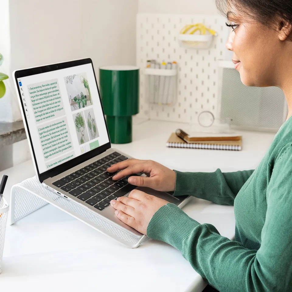 Person using green laptop on raised stand in organised workspace.