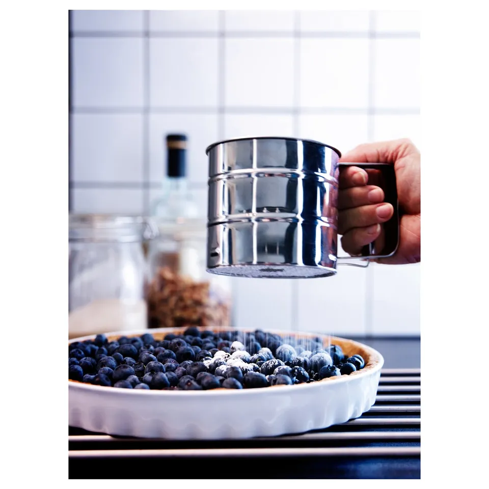 Person dusting blueberries with icing sugar using a silver shaker.