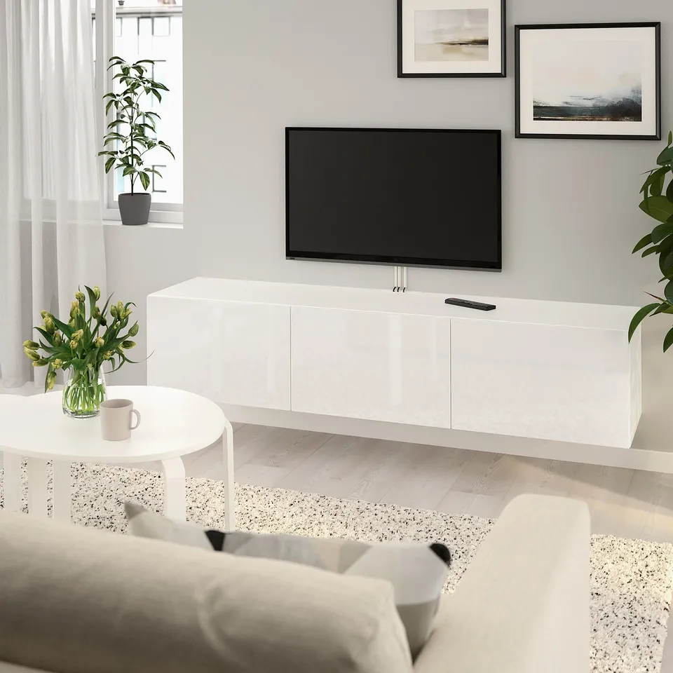 Modern living room with BESTÅ tv bench, flat-screen tv, storage drawers, large window, small coffee table with plant and flowers, light-colored sofa.
