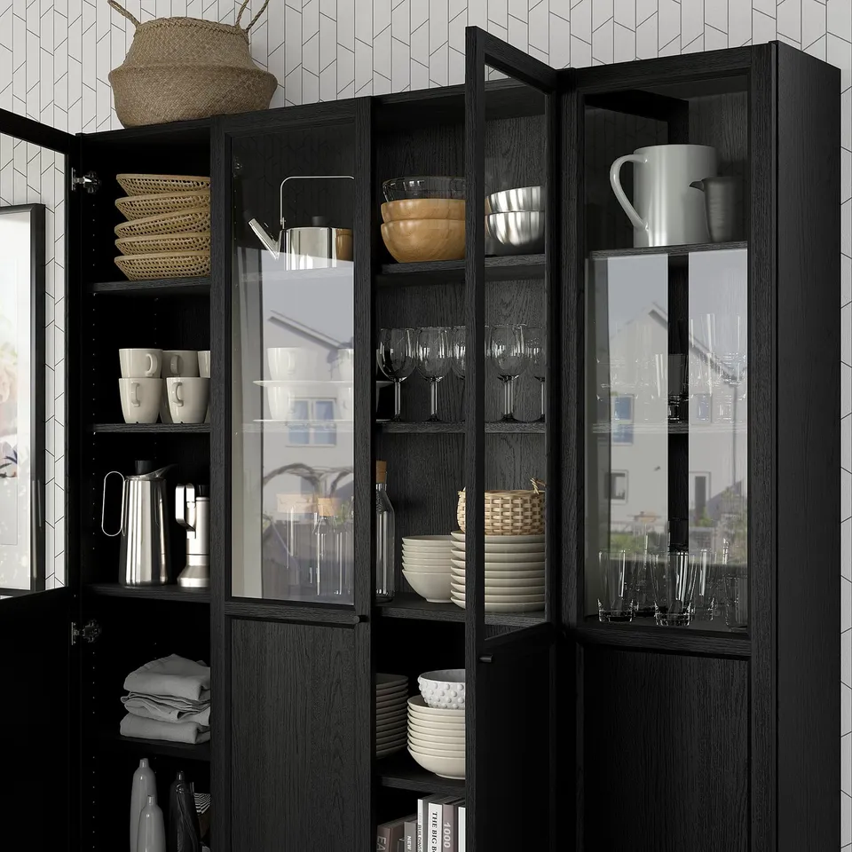 Black BILLY bookcase with glass and panel doors, displaying dishes, cups, and baskets. Adjustable shelves.