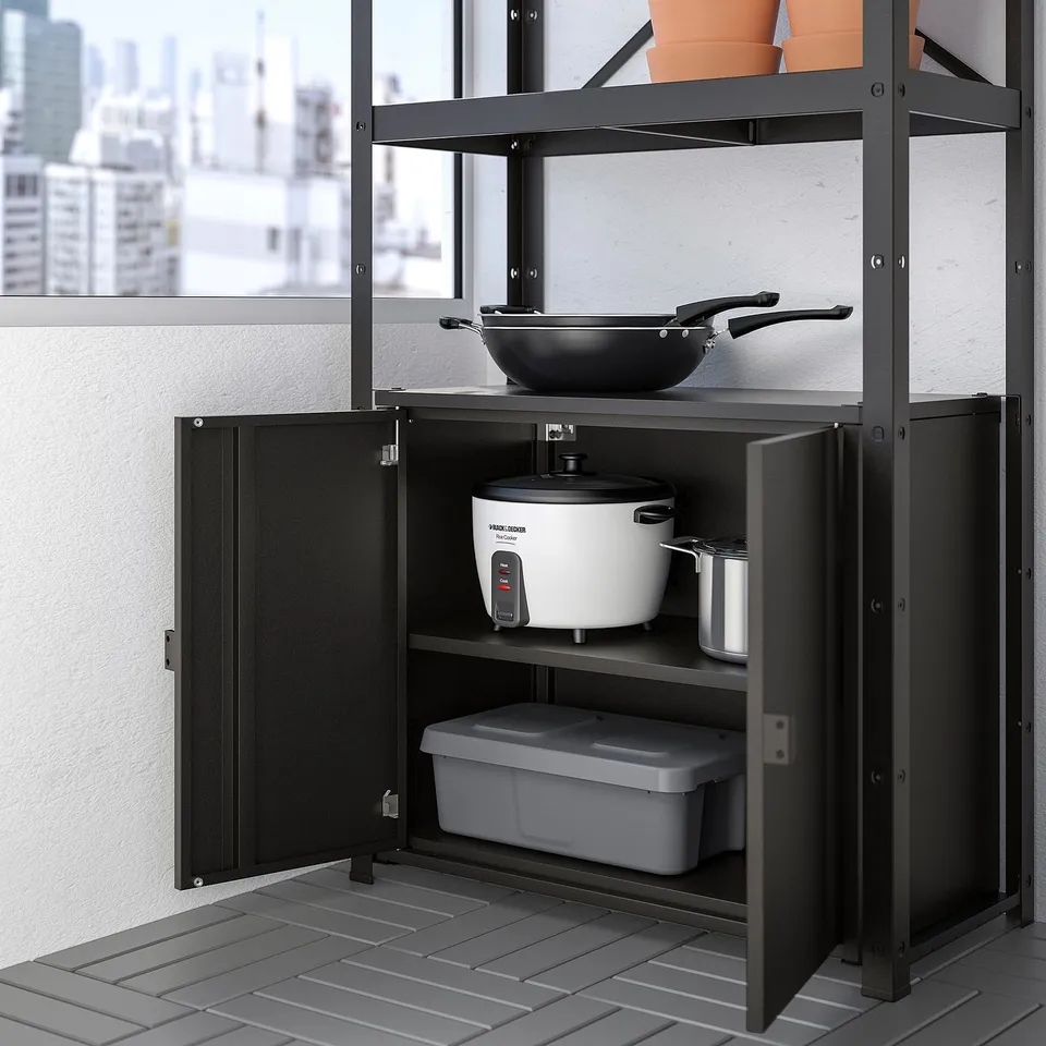 Metal storage shelf with open door revealing rice cooker, canister, and plastic box; upper shelf holds frying pan.