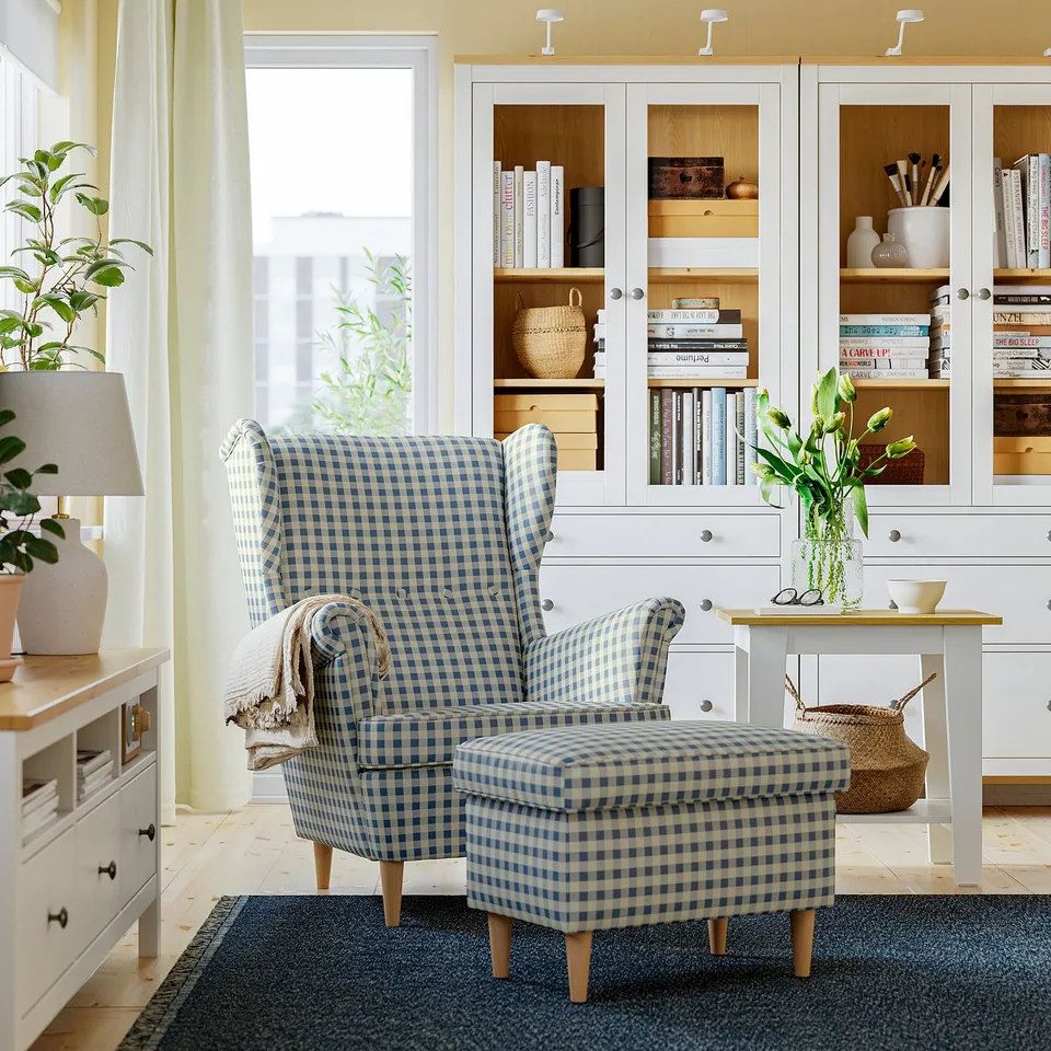 Blue & white STRANDMON chair & ottoman in cosy living room with bookshelf and window.