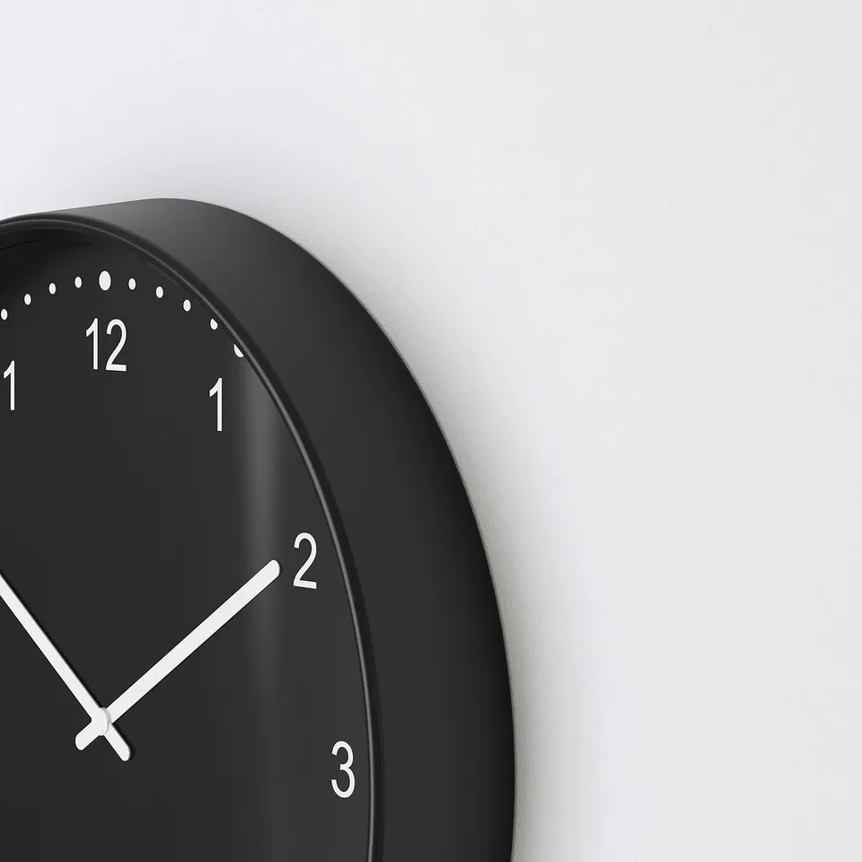 Black circular clock with white numbers and hands, showing time as 1:53 on a plain light wall.