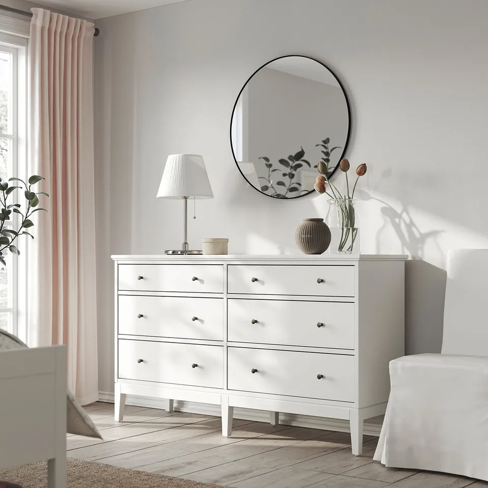 Minimalist white dresser, round mirror, lamp, and vase with flowers. Soft-close drawers, light-filled room.