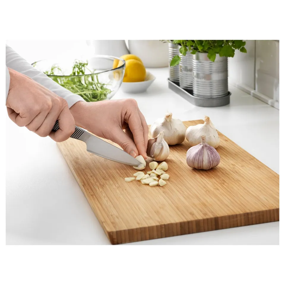 Person chops garlic on a wooden cutting board using a small knife.